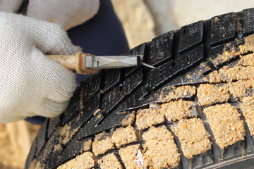 Repairman hand in a white work glove removes a screw from punctured car tire with a pliers