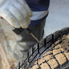 A hand in a work glove cleans the wheel puncture with an awl