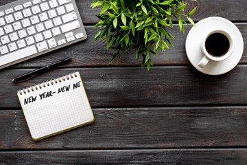 New year new me motto - motivation concept. Notebook for writing goals and plans on dark wooden office desk top-down copy space