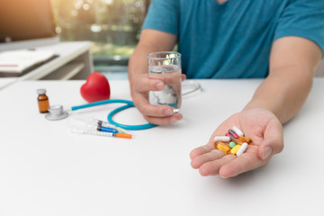 Young man holding assorted pharmaceutical medicine pills in one hand and glass of water in other one
