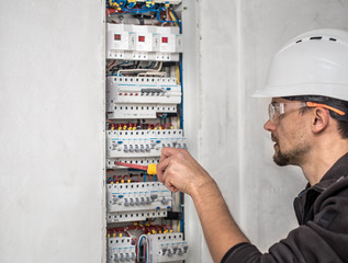 Man, an electrical technician working in a switchboard with fuses. Installation and connection of electrical equipment.