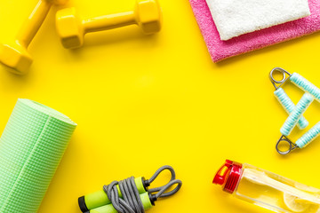 Fitness background - dumbbells, jump rope, sport carpet, water bottle - on yellow top-down frame copy space