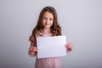 Naklejka premium beautiful little brunette girl with a white sheet of paper on a white background, smiling, surprised