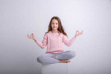 a little brunette girl sits on a cube in a meditative pose isolated on a white background