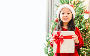 Little asian girl smile and excited and holding red gift box on christmas tree and white background.Child girl holding gift box in Christmas celebration and Happy New year concept.