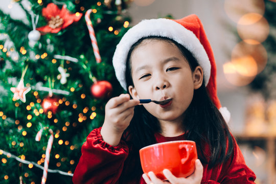 Asian kid girl eating ice cream on christmas celebration season with christmas tree background at home.Child girl enjoy eating and hungry concept.