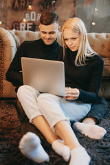 Portrait of a charming young couple dressed in black sitting on the floor and looking to a laptop screen.