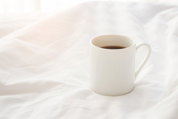 Black coffee cup on the unmade bed in cozy morning with sunshine into window.