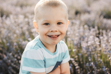 Close up portrait of a cute little kid looking at camera smiling show tongue against a field of flowers.