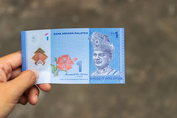 One Ringgit Malaysia bank note on hand isolated on grey background.