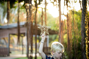 Young boy holding gold Christmas star up in the air with natural sunlight streaming through