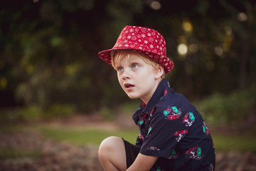 Cute little boy sitting in park wearing Christmas outfit including Santa hat