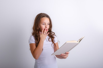 Teenage girl with a book in her hands on a white background. Shows emotions  surprise, sadness.