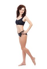 Fototapeta premium A barefoot girl in a black sports swimsuit is standing on a white background.