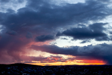Blue-red sunset with dark gloomy clouds over the city. Dark silhouette of the city with a beautiful blurred dawn. Artistically blurry