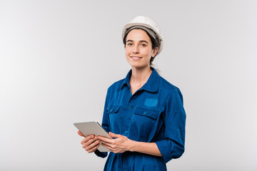 Smiling successful female engineer in workwear and hardhat using touchpad