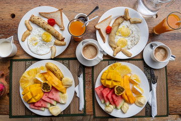 Fototapeta na wymiar Tropical breakfast of fruit, coffee and scrambled eggs and banana pancake for two on the beach near sea. Top view, table setting.