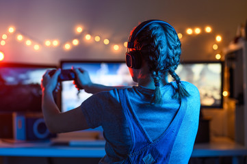 Gamer or streamer girl at home in a dark room with a gamepad playing video games with friends...