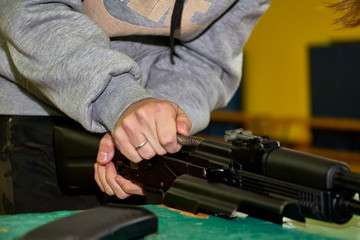 Hands of young person is dismantling a weapon. Teenager collects a Kalashnikov assault rifle on the...