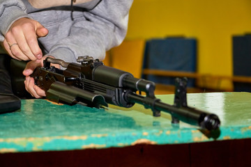 Hands of young person is dismantling a weapon. Teenager collects a Kalashnikov assault rifle on the...