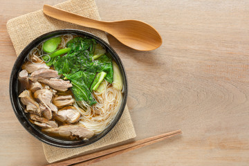 top view of rice vermicelli soup with sliced duck meat in a ceramic bowl on wooden table. delicious food menu.