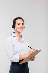 Young smiling elegant businesswoman in headset making notes in document