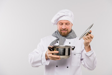 Young professional male chef looking at tasty soup or other cooked meal in pan