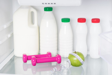 bottles with kefir and milk stand on a shelf behind pink dumbbells and a green apple in the...