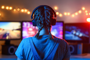 A girl plays video games at a computer. on the background of three monitors. Creative light - obrazy, fototapety, plakaty