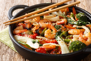 One pot stir fried shrimp, squid and mussels with fresh vegetables close-up in a pan on the table....