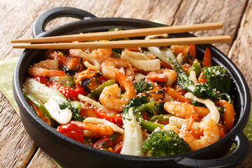 Asian stir fried shrimp, squid and mussels with fresh seasonal vegetables close-up in a pan. horizontal