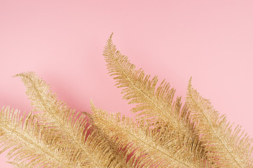 Gold and pink festive background - sparkling glittering fern branches on soft light pastel pink background, border, copy space, top view.