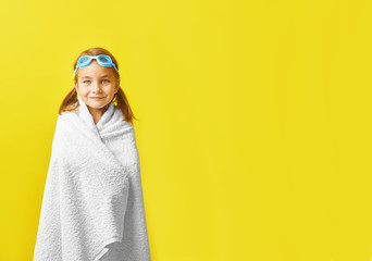 Funny happy child in swimsuit and swimming glasses , wrapped in a towel, on colored background.