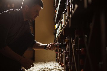 Sommelier taking one of bottles from wooden cellar