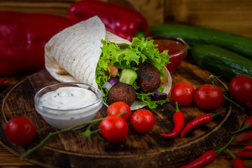 Falafel and fresh vegetables in pita bread on wooden table
