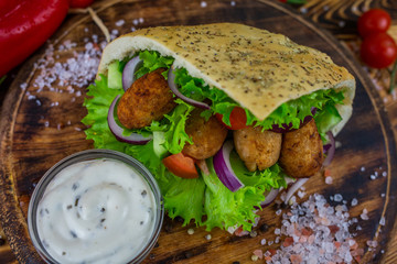 Falafel and fresh vegetables in pita bread on wooden table