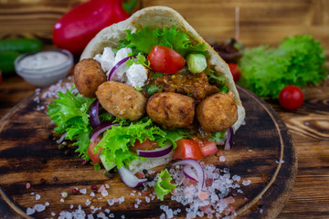Falafel and fresh vegetables in pita bread on wooden table