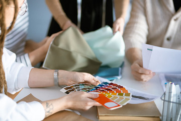 Hands of designer holding color palette over desk while working with colleagues