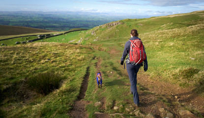 A female hiker walking their dog along a rough trail leading from High Cup Nick towards Dufton.