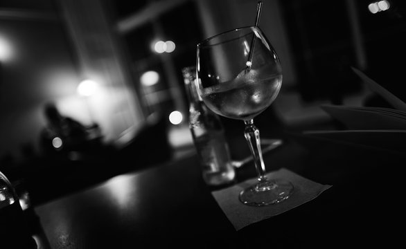 A black and white image of a gin and tonic on a dimly lit bar.