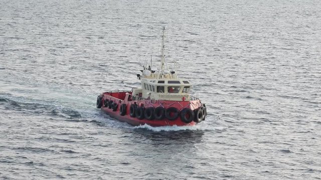 small towboat with tyre protected boat sides moves fast in direction to tanker Onyx crossing grey sea water
