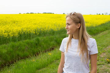 Naklejka na ściany i meble The girl looks into the distance of the yellow field and the blue sky. Summer mood and girl's dreams