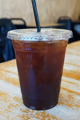 Close up take away plastic cup of iced black coffee on wooden table