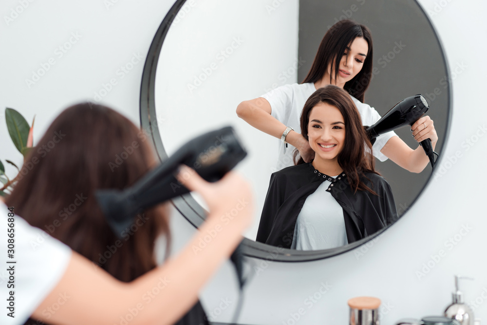 Wall mural cute beautiful girl with long hair looks in the mirror, she came to the beauty salon, her hairdresse