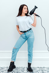 Charming girl with hairdryer in hand posing on a white background