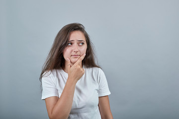 Young girl in white t-shirt over gray isolated wall ponders idea holding hand on chin