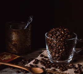 Roasted coffee beans in a clear cup of coffee on burlap and wood. Dark mood coffee beans photography.