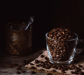 Roasted coffee beans in a clear cup of coffee on burlap and wood. Dark mood coffee beans photography.