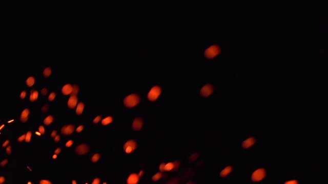 Fire flames with flying sparks on a black background. Firestorm texture. Bokeh lights on black background, flying fire sparks in the air. Sparks from bonfire over dark night background. Slowmo