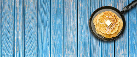 Fototapeta na wymiar Hot delicious pancakes in frying pan on blue wooden table. Pancake week. Panoramic banner.